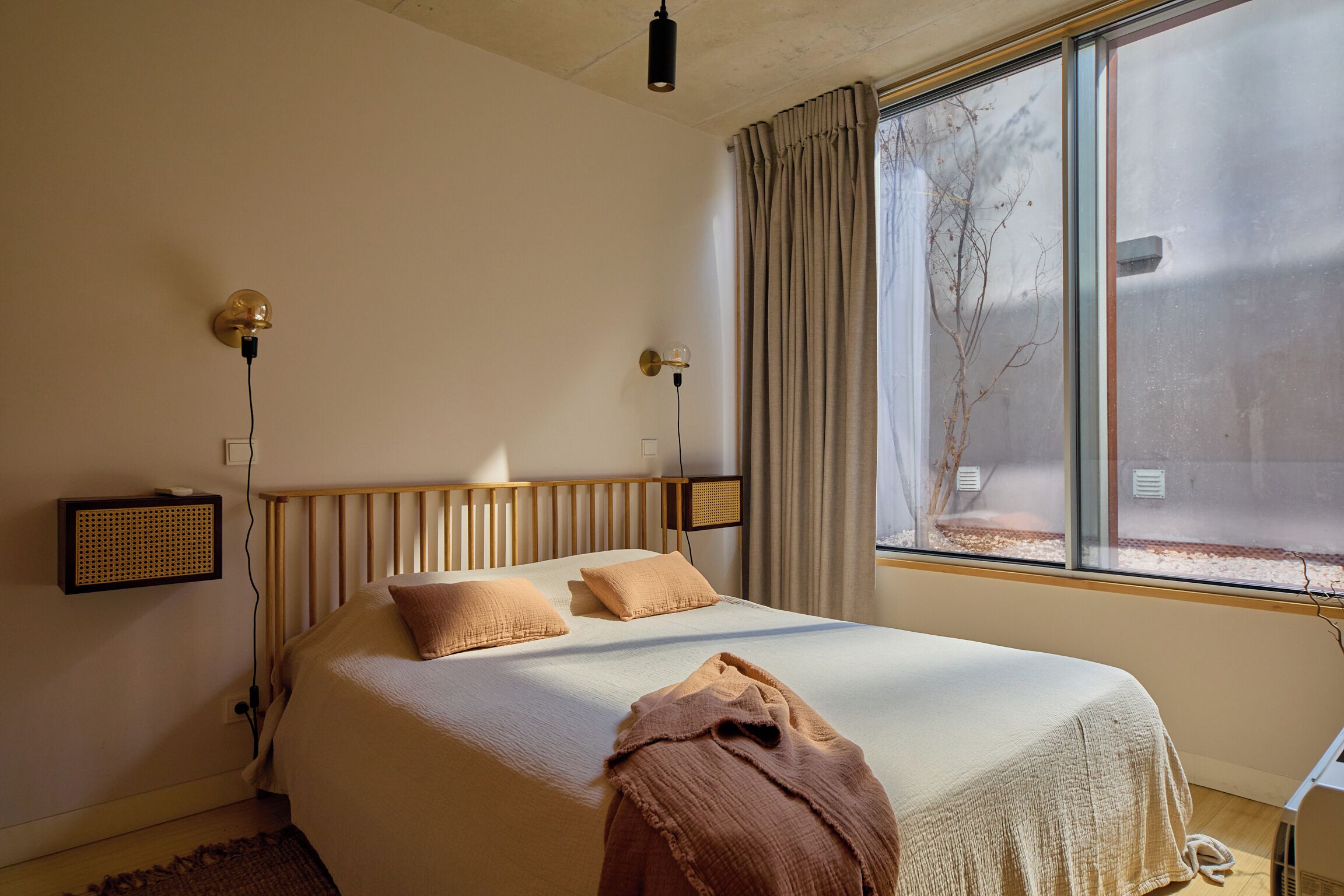 A bedroom with a large bed, a radiator, a window with curtains, and a wall-mounted lamp.
