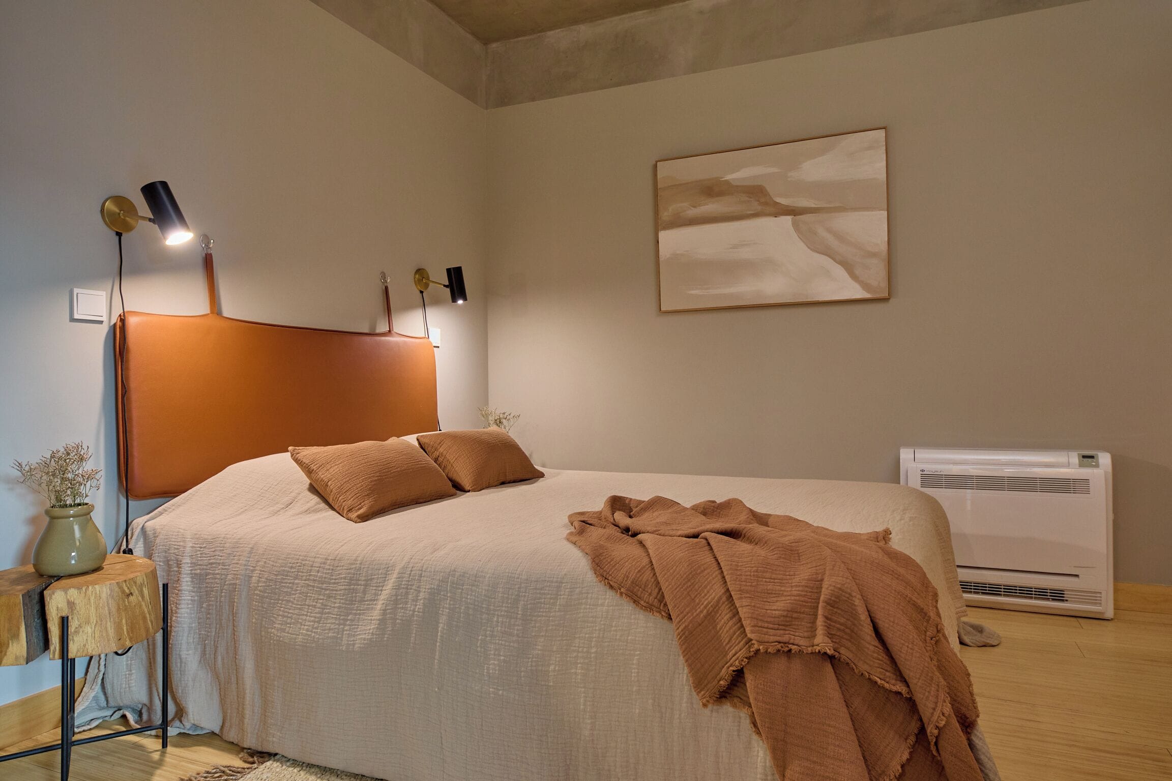 Un dormitorio con una cama, lámparas de noche, aire acondicionado instalado en la pared y un cuadro.