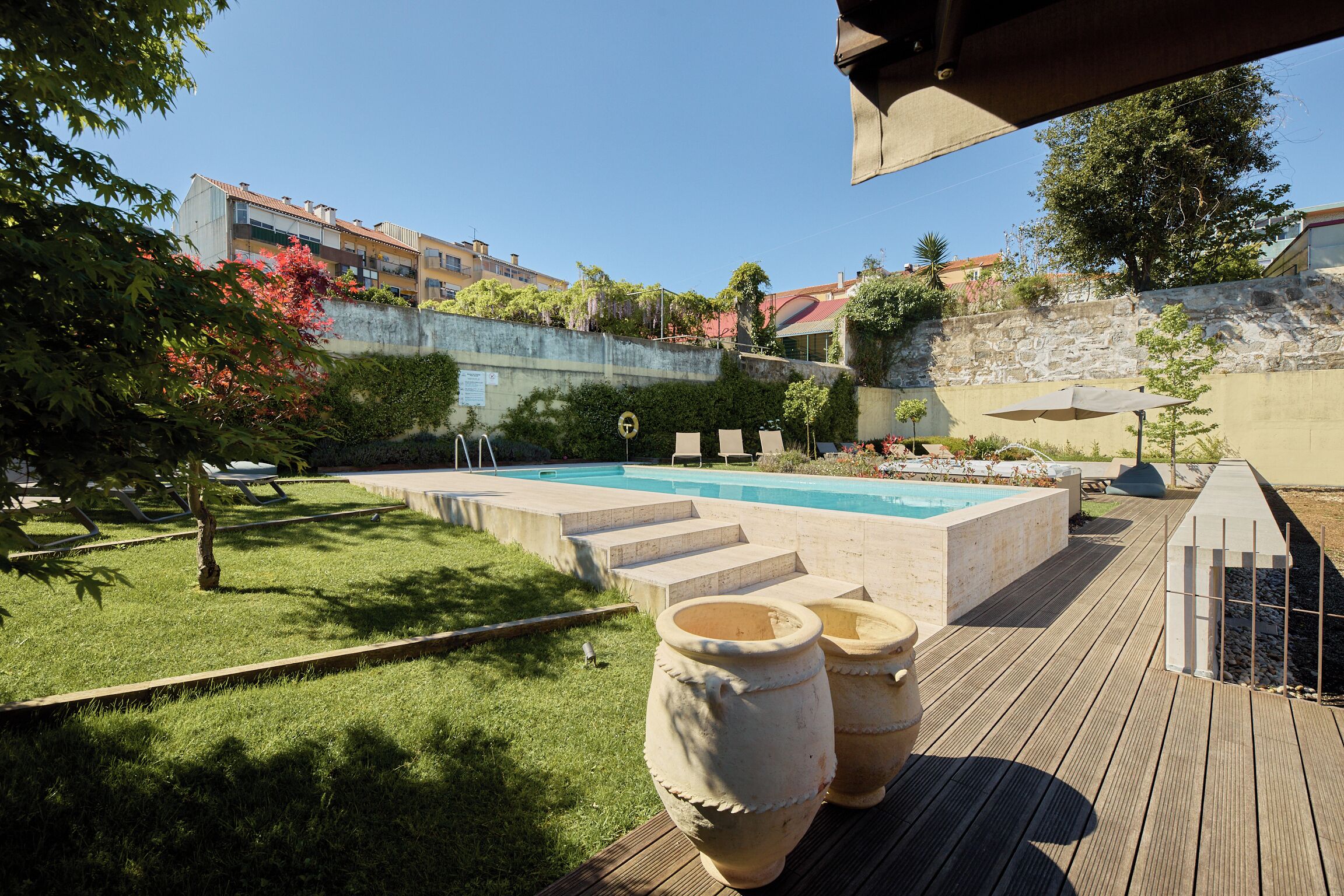 Una piscina con gradini d'accesso, circondata da un solarium in legno e piante in vaso.