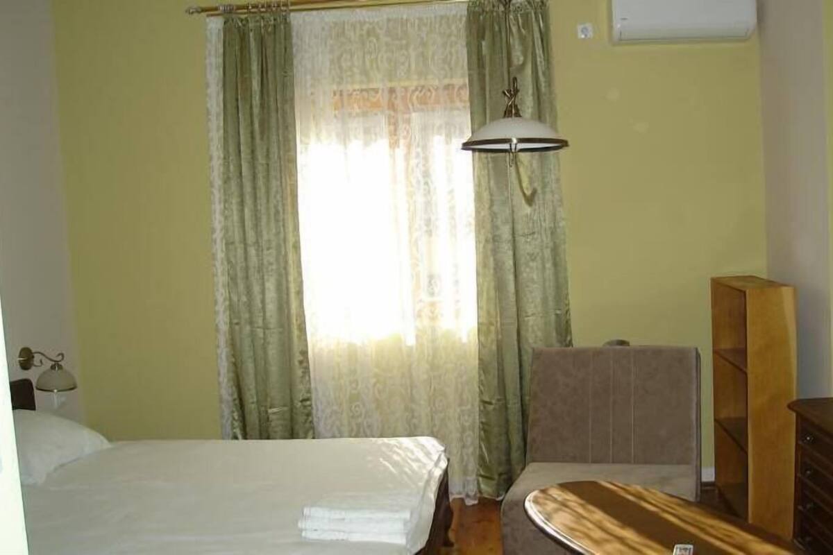 A room with a bed, a wooden dresser, a desk, and a lamp.