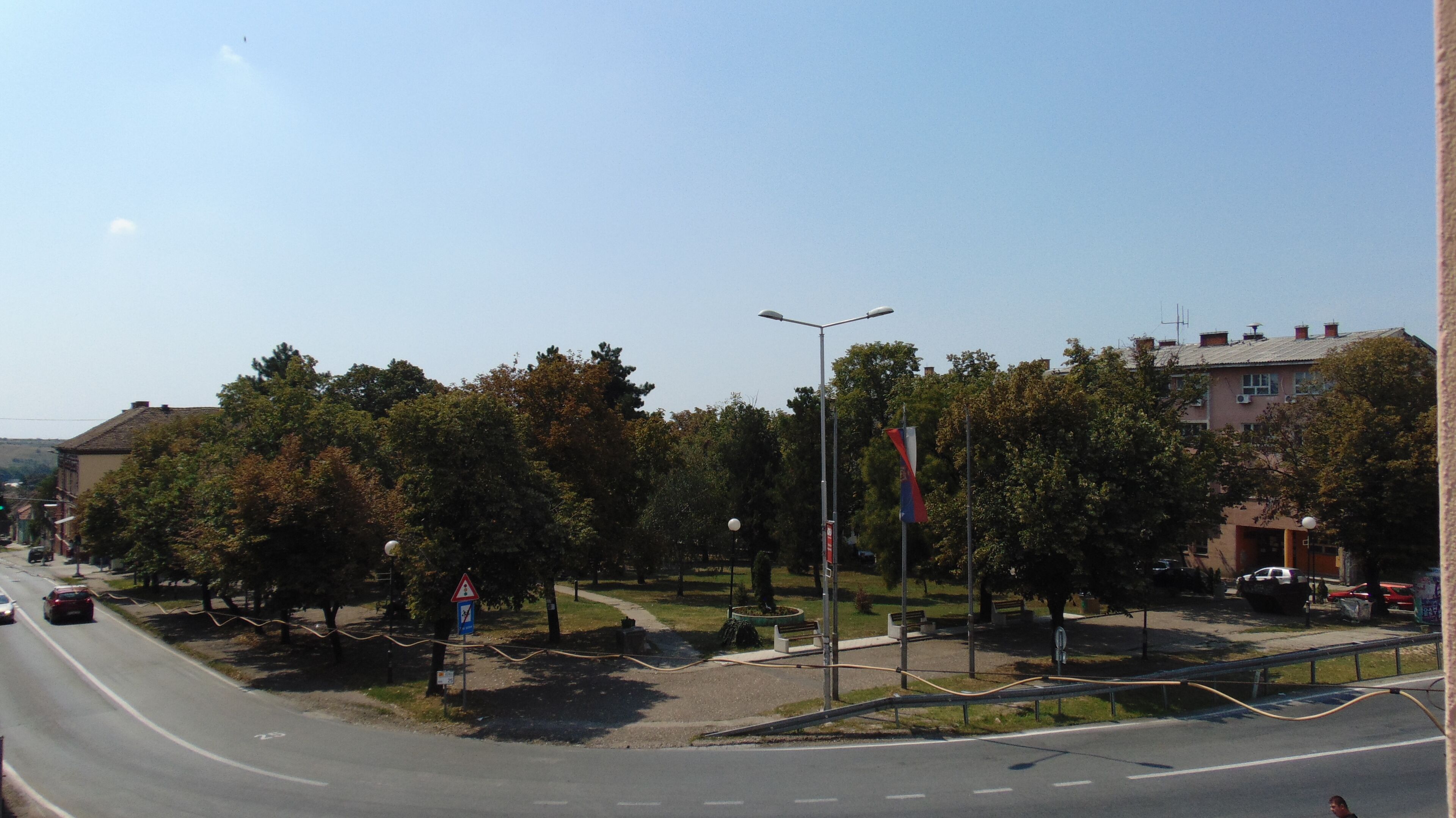 Straßenansicht mit Kreisverkehr, Bäumen und Gebäuden.