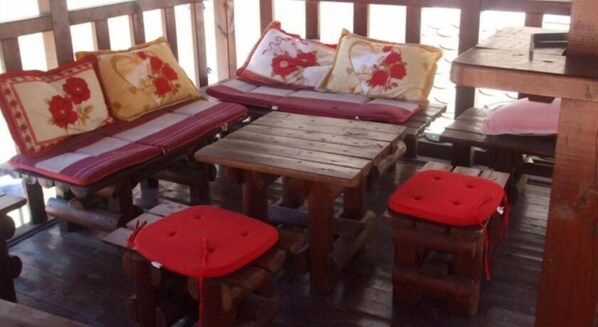 Terraza de madera con un conjunto de sofá y dos taburetes pequeños, cada uno con cojines rojos.