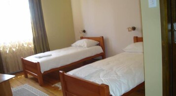 Duas camas de solteiro em madeira com roupa de cama branca num quarto com soalho em madeira e janela com cortinas.