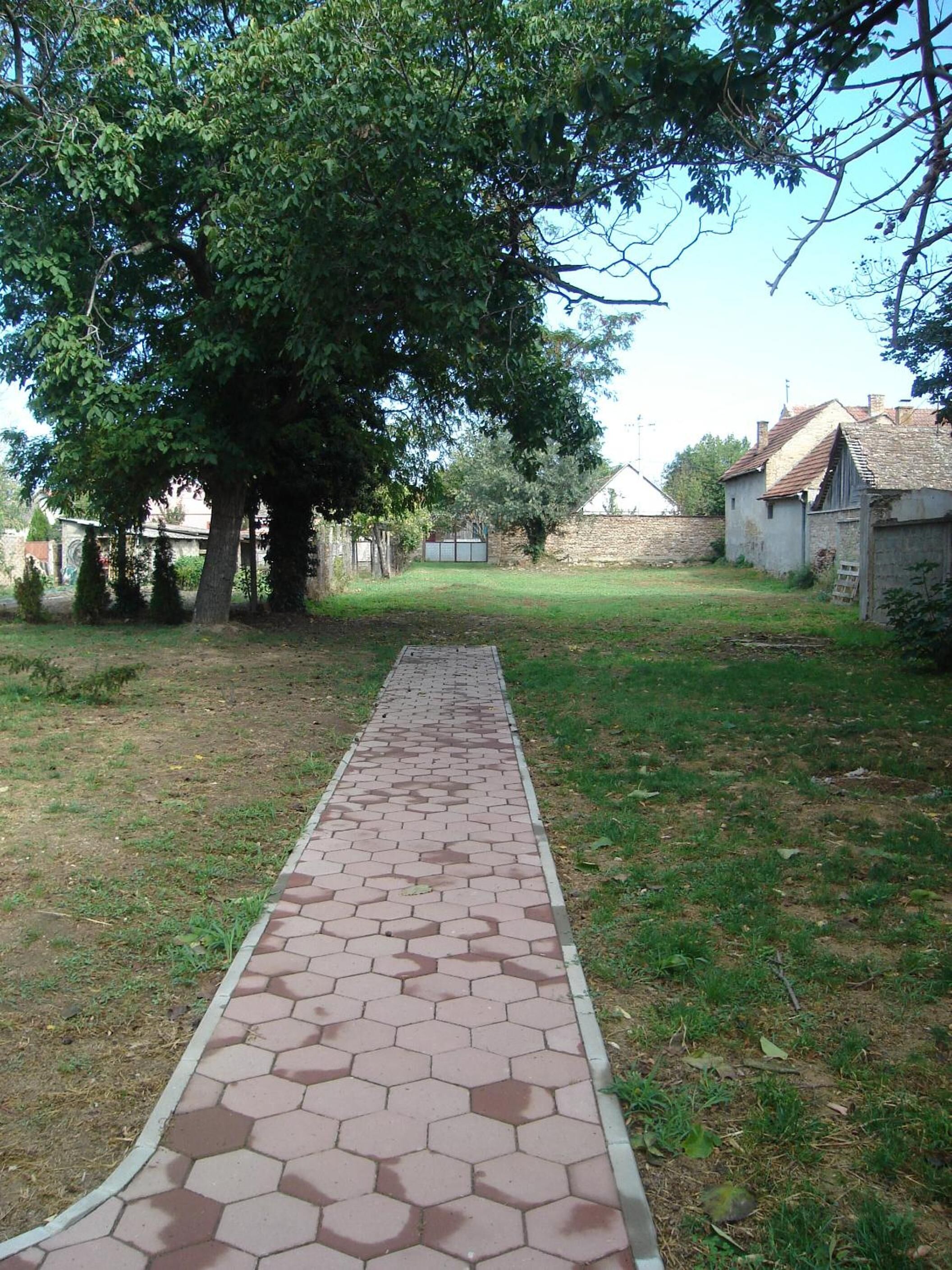 Un sendero pavimentado que conduce a un edificio con un muro de piedra y un camino bordeado de árboles.