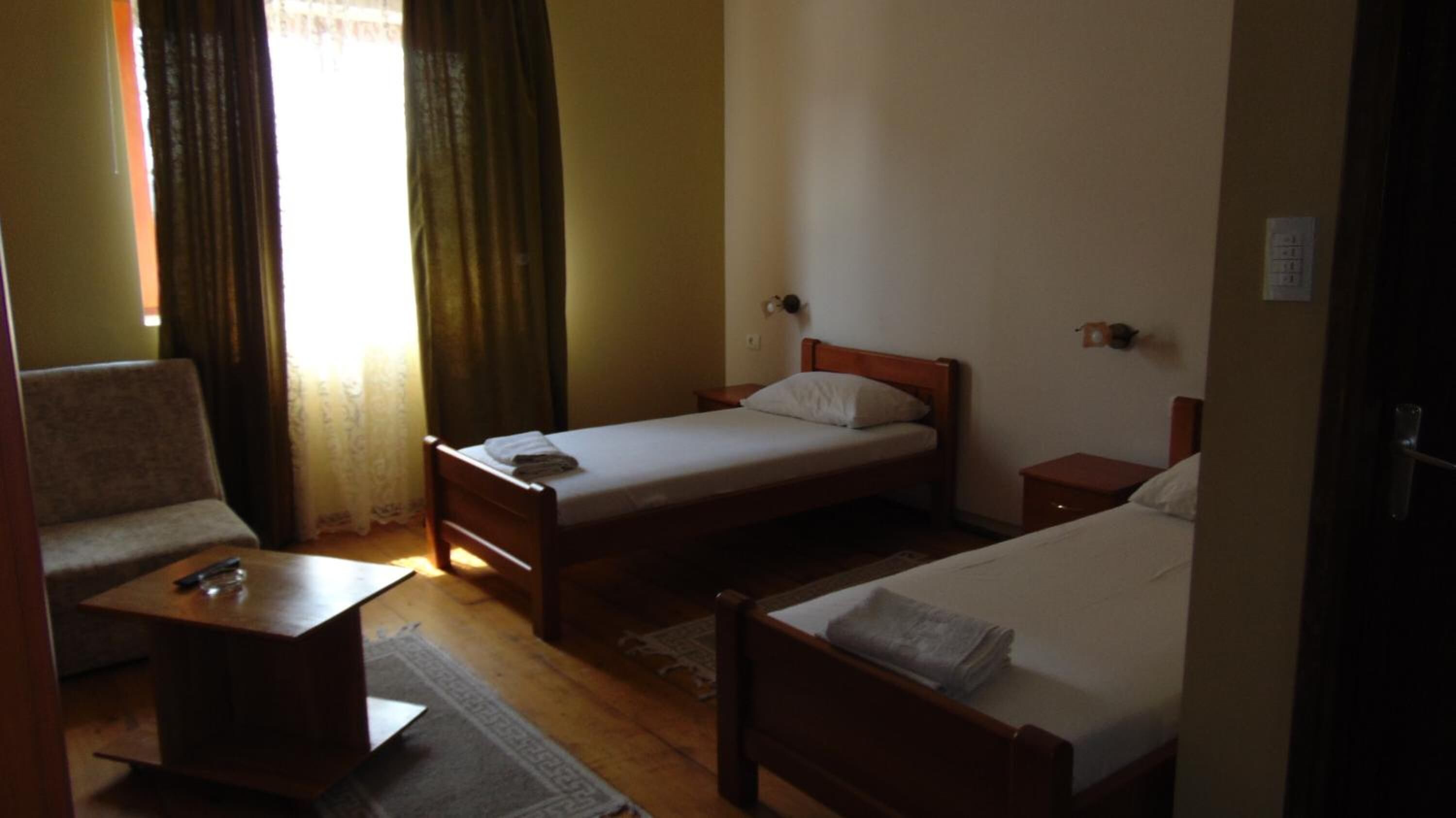 A room with two single beds, a small table, a chair, and a window with curtains.