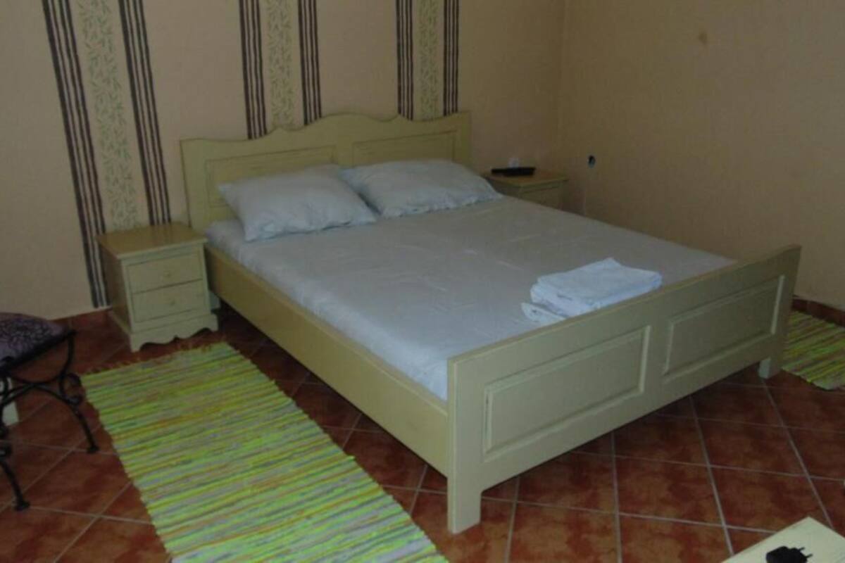 A bedroom with a bed, nightstands, a chair, and a striped rug.