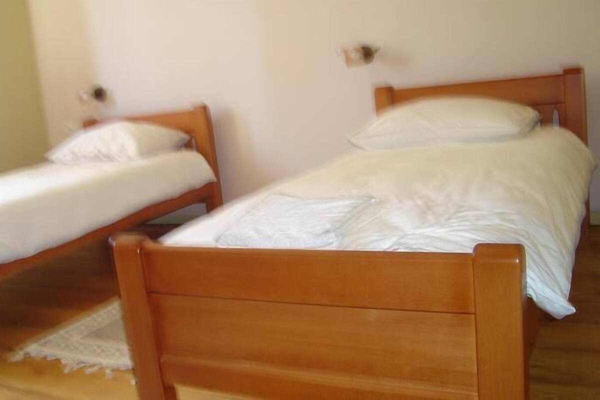 Two wooden beds with white linens in a room with plain walls and a wooden floor.