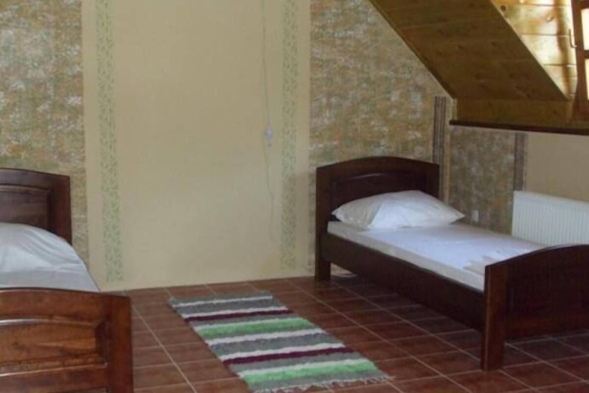 A room with two wooden beds, a striped rug, and a sloped ceiling.