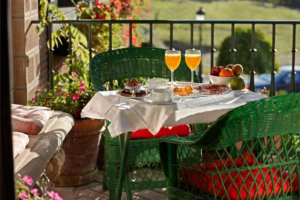 A table set outdoors with a white tablecloth, two glasses of orange juice, a bowl of fruit, pastries, and a teapot.