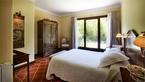 A bedroom with a large bed, a wooden wardrobe, a chair, a desk, and a window with curtains. - Hotel Ibarra (Zalla)