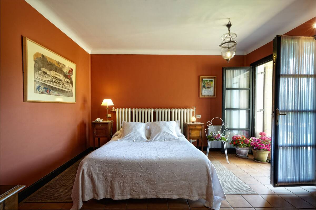 A bedroom with a bed, a nightstand, a lamp, a chair, and a window with curtains.
