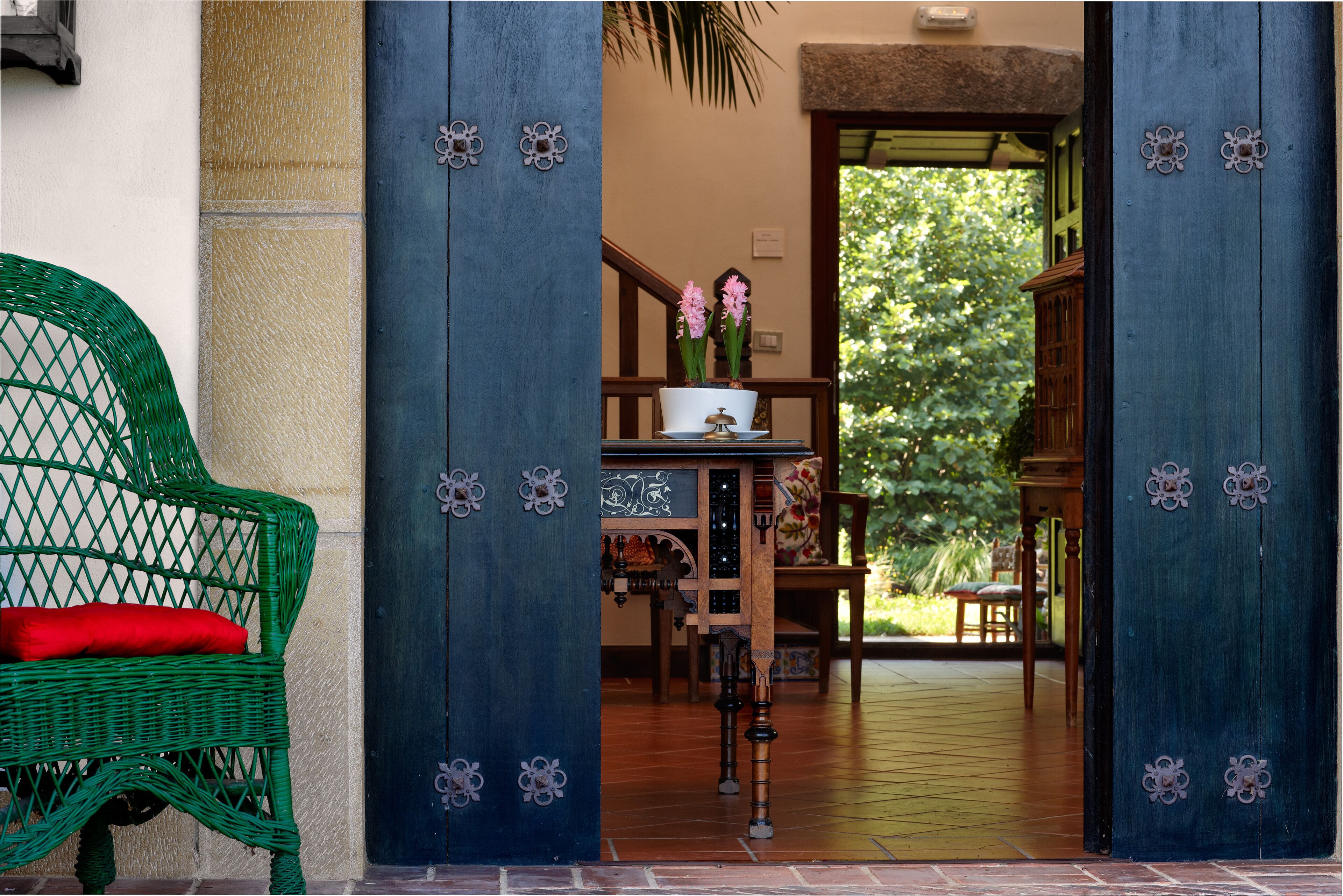 A green wicker chair with a red cushion outside a door with decorative metal handles.
