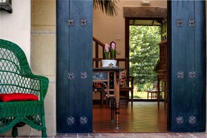 A green wicker chair with a red cushion outside a door with decorative metal handles. - Hotel Ibarra (Zalla)