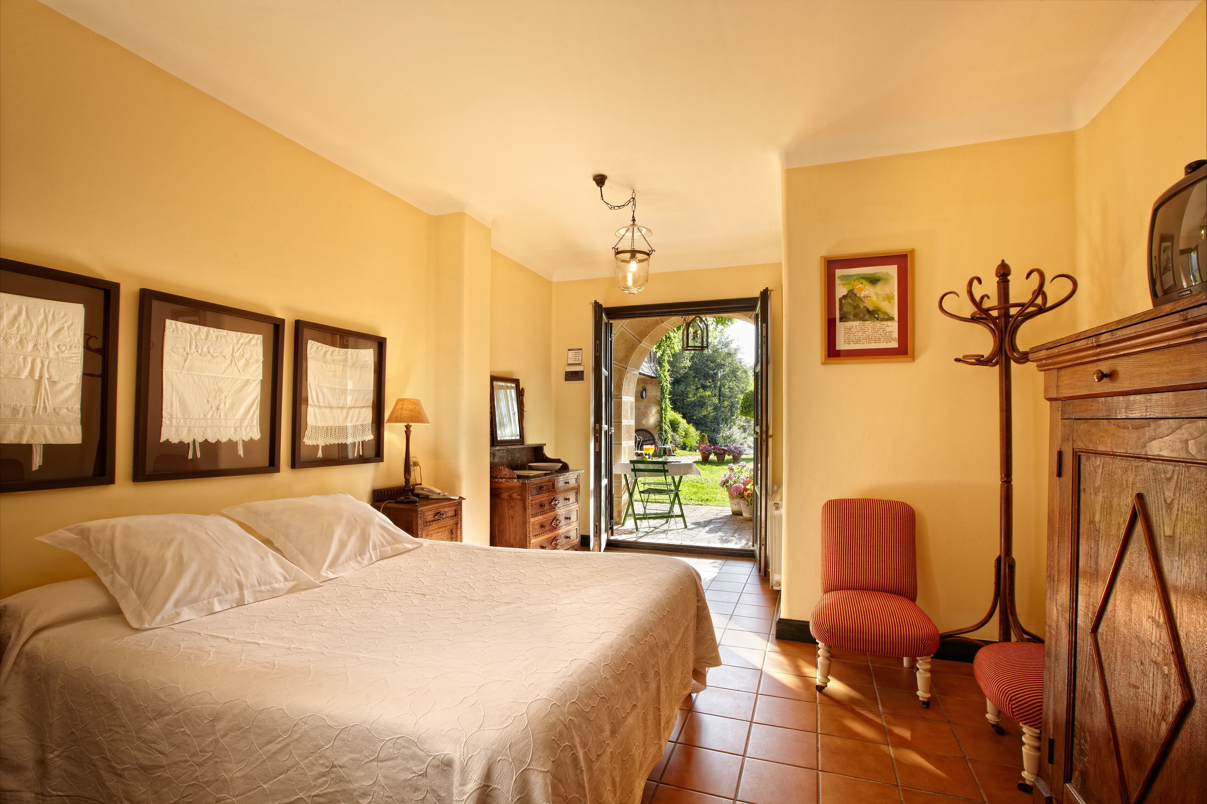 A bedroom with a bed, a chair, a dresser, and a door leading to a garden.
