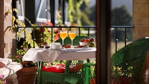 Una mesa dispuesta con alimentos para el desayuno, incluyendo frutas y bebidas, en un balcón con vista a la vegetación.