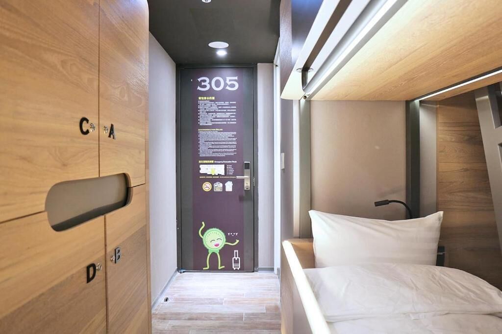 A modern hotel room with a wooden wardrobe, a bed with white bedding, and a door with a number 305 sign and a cartoon character.