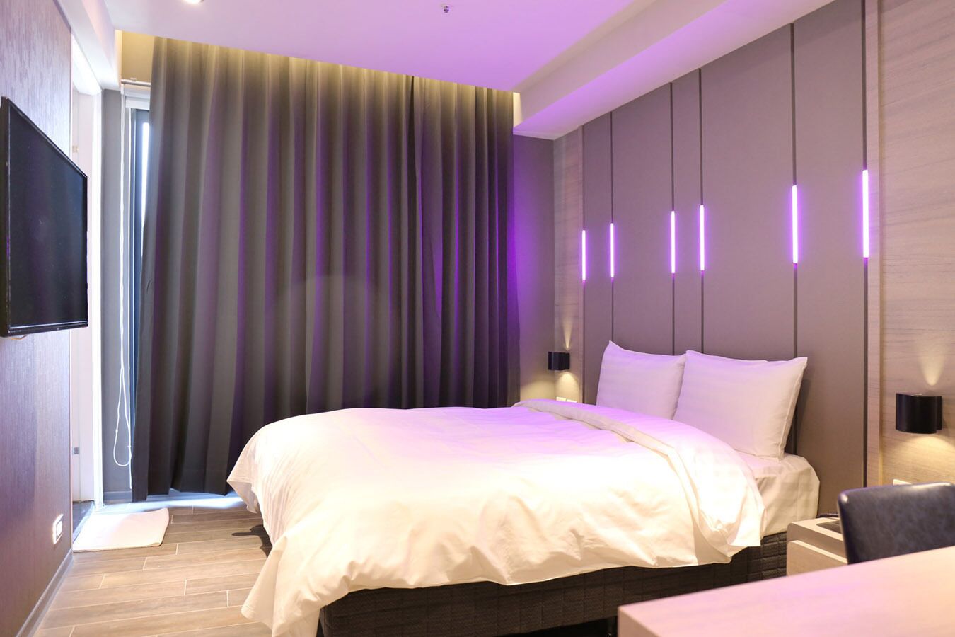 Una habitación de hotel moderna con una cama grande, un televisor de pantalla plana e iluminación ambiental.
