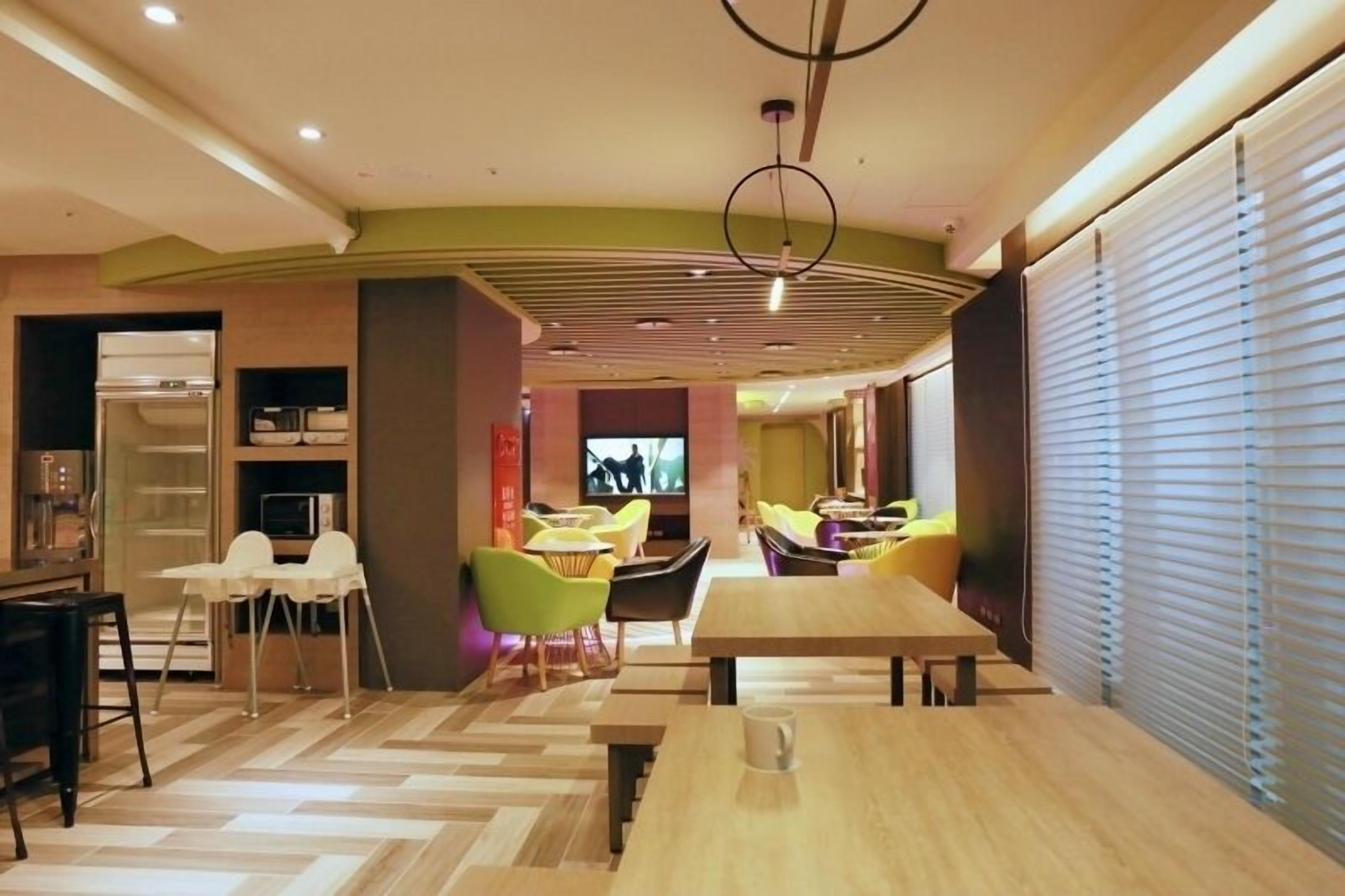 Un comedor moderno con mesas y sillas de madera, un televisor y una zona de cocina con electrodomésticos.