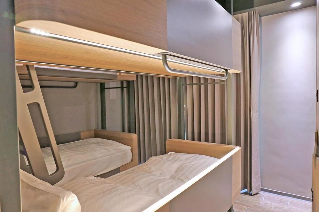 Una habitación de hotel moderna con dos camas individuales, un cabecero de madera y una ventana cubierta por cortinas.