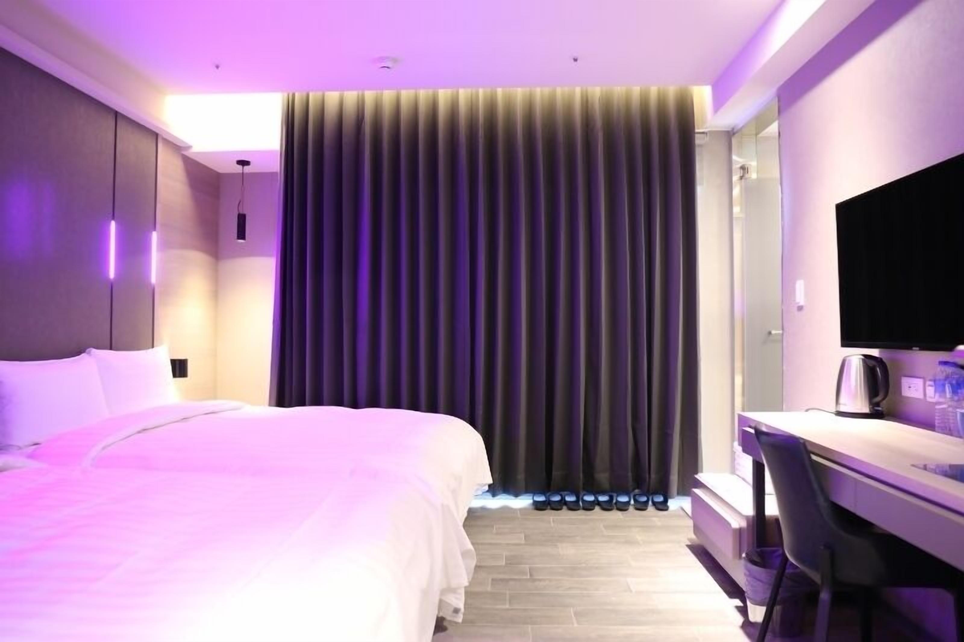 A hotel room with a bed, a desk, a chair, and a TV.