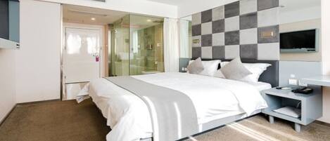 Une chambre d’hôtel moderne dotée d’un grand lit, d’une table de chevet, d’une télévision et d’une douche en verre.