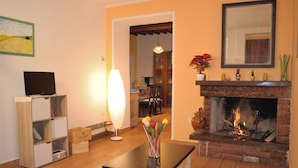 A living room with a fireplace, a television on a stand, and a table with a vase of flowers.