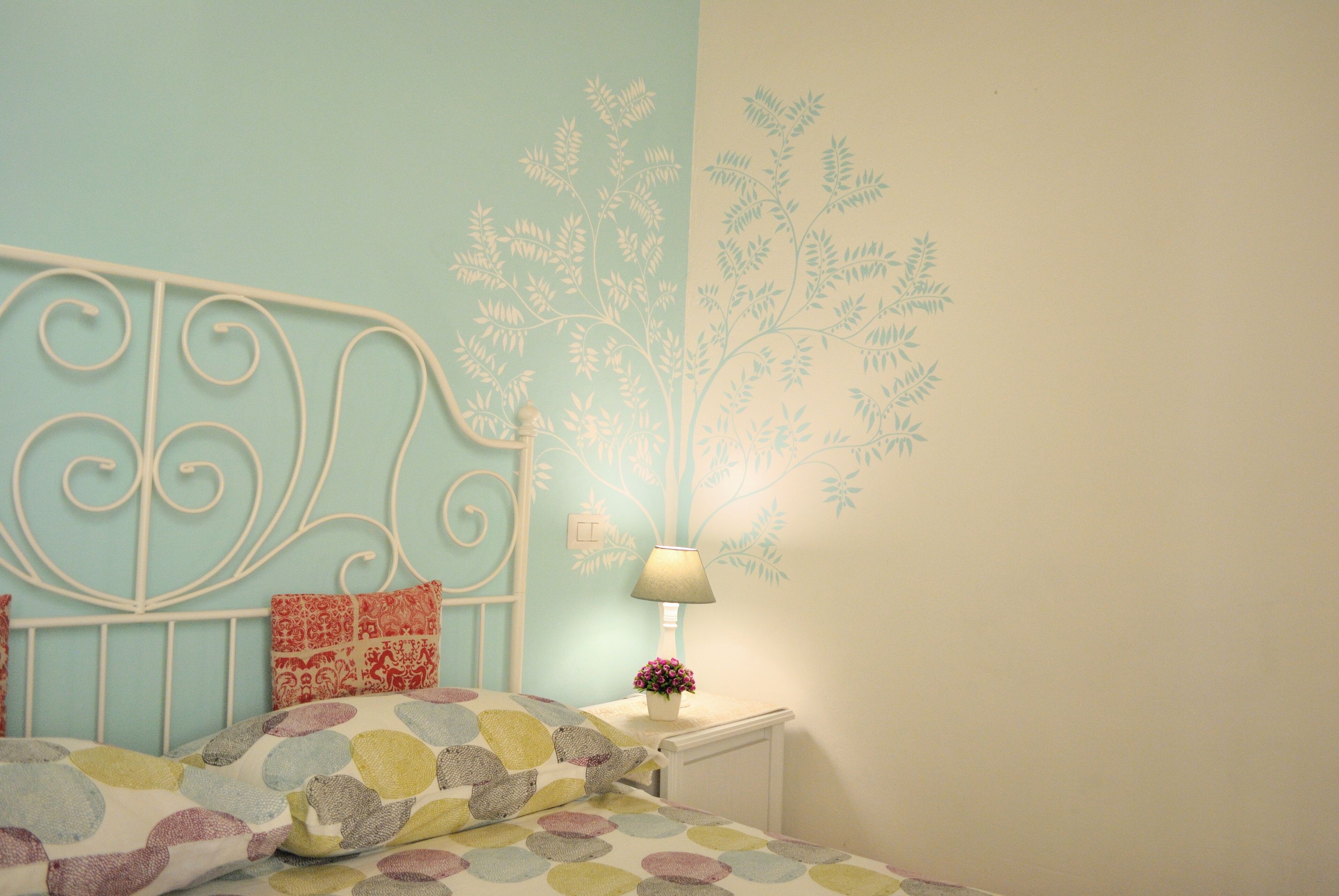 A bedroom with a bed, a nightstand, a lamp, and a wall mural.