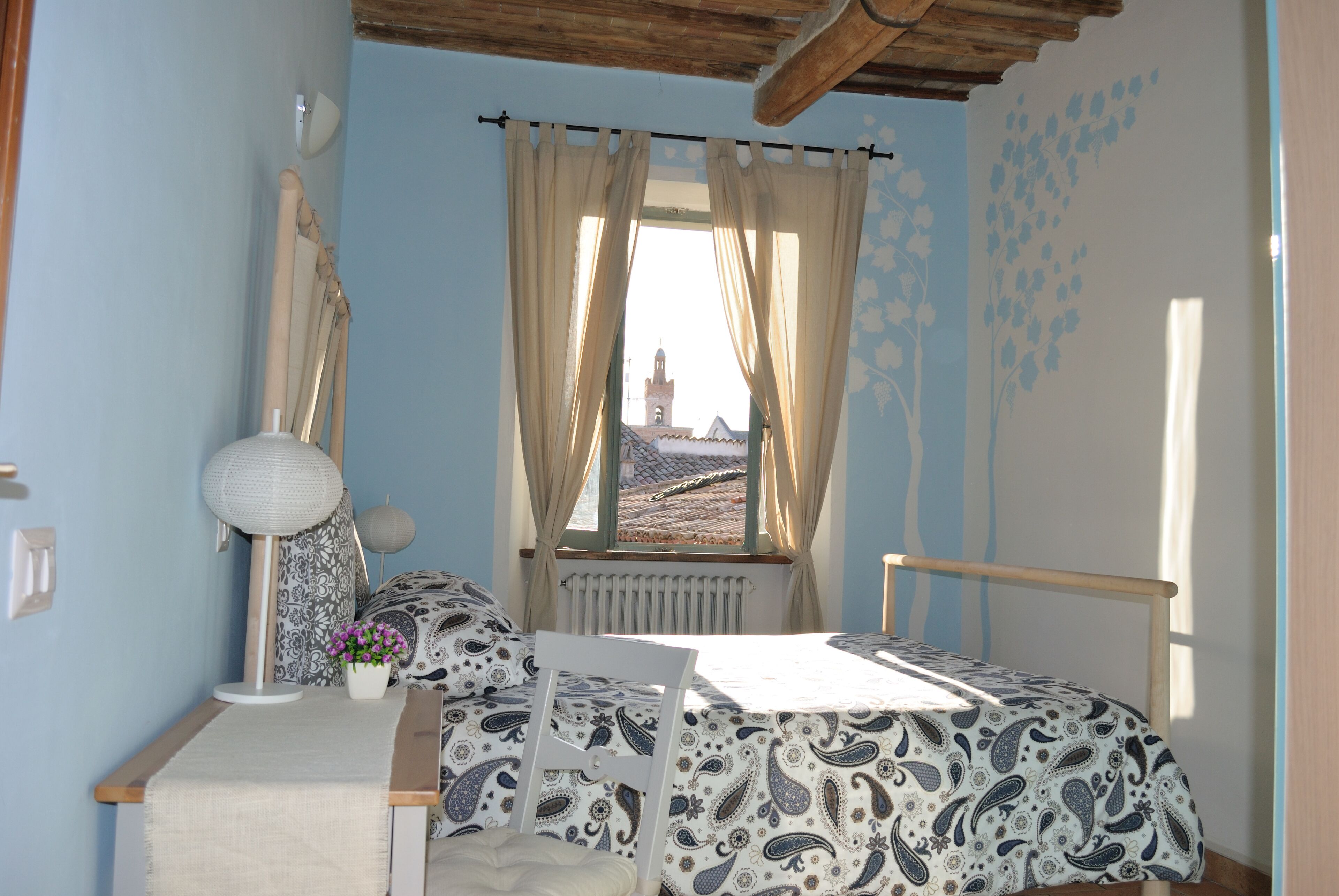 A bedroom with a bed, a chair, a table, a lamp, and a window with curtains.