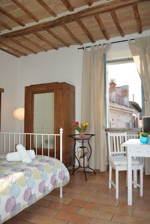 A room with a bed, a small table with a vase of flowers, a chair, and a window overlooking a building. - Cozy 4-bedroom apartment with lovely terrace (Foligno)