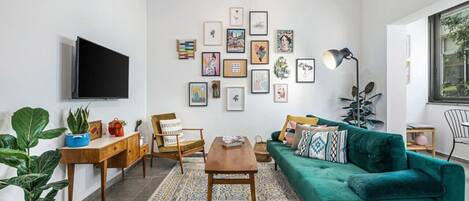 A modern living room with a teal sofa, wooden coffee table, and a variety of framed artworks on the wall.
