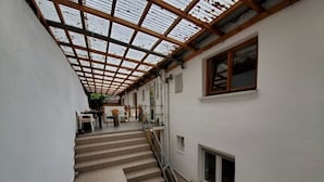A corridor with a staircase leading to an upper floor, a covered area with a wooden ceiling, and a white wall with a window and a small vent. - Zum Odenwald (Gorxheimertal)