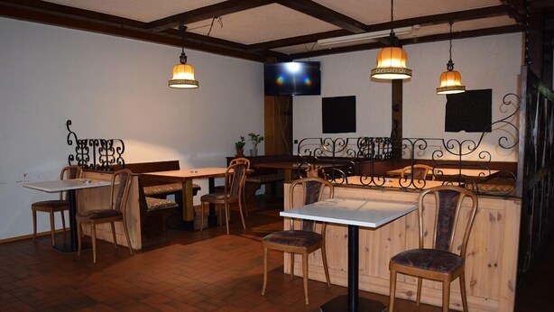 A restaurant with wooden tables and chairs, a TV mounted on the wall, and pendant lights. - Zum Odenwald (Gorxheimertal)