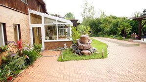 A brick pathway leading to a building with a glass entrance. There is a stone frog sculpture in the center of a grassy area. - Nichtraucher-Pension Zum Froschkönig (Lübbenau/Spreewald)