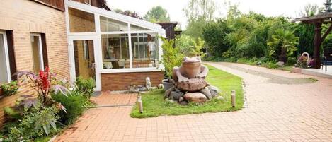A brick pathway leading to a building with a glass entrance. There is a stone frog sculpture in the center of a grassy area.