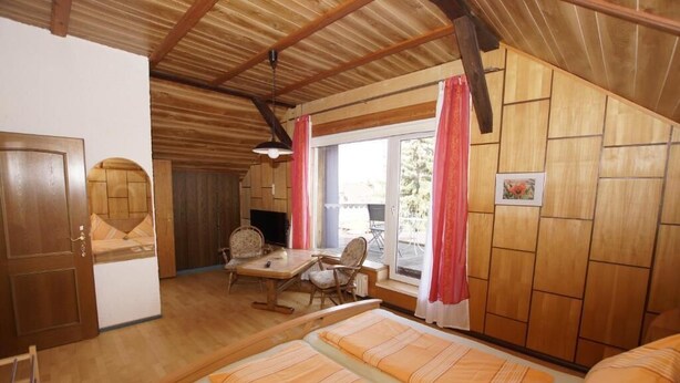 A room with two beds, a wooden ceiling, a dining table with chairs, a window with curtains, and a door. - Nichtraucher-Pension Zum Froschkönig (Lübbenau/Spreewald)
