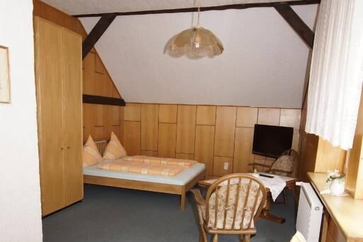A cozy attic bedroom with a bed, a chair, a table, and a hanging light fixture.