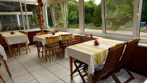 A restaurant with wooden tables and chairs, large windows, and a view of greenery outside. - Nichtraucher-Pension Zum Froschkönig (Lübbenau/Spreewald)