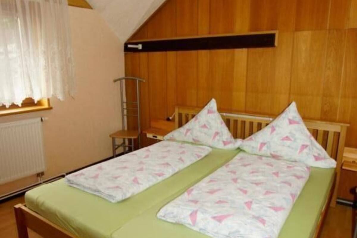 A room with a wooden bed, a window with white curtains, and a radiator.