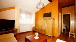 A living room with a wooden floor, a television, a wooden cabinet, and a small table with a vase. - Nichtraucher-Pension Zum Froschkönig (Lübbenau/Spreewald)
