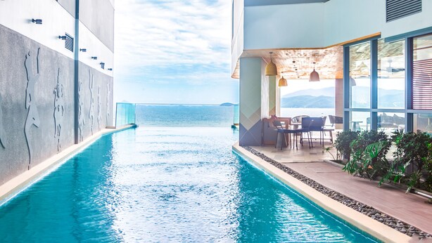 A modern indoor pool with a view of the sea, surrounded by a lounge area with seating and plants. - OPOX Panorama (Nha Trang)