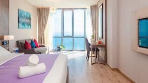 A hotel room with a bed, a desk, a chair, and a large window offering a view of the sea. - OPOX Panorama (Nha Trang)