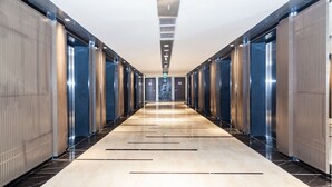 A long, narrow hallway with a polished floor, flanked by tall, metallic elevator doors and walls. - OPOX Panorama (Nha Trang)