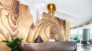A reception area with a modern design, featuring a large reception desk, a wall with a wood grain pattern, and a large chandelier. - OPOX Panorama (Nha Trang)
