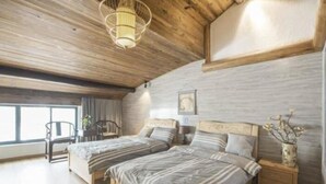 A bedroom with two beds, wooden flooring, a ceiling light, a window, and a nightstand with a vase.