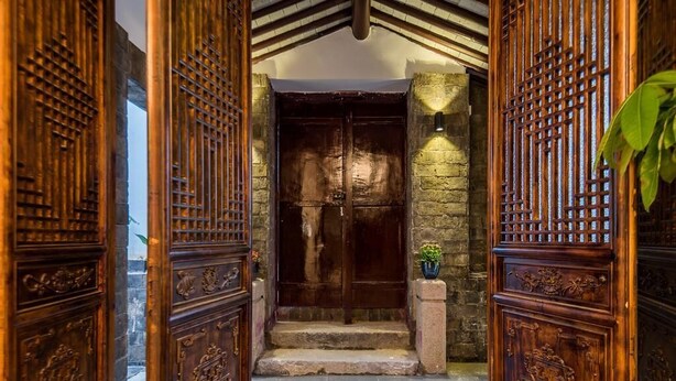 A wooden entrance with a large door and intricate carvings, leading to a stone wall and steps.