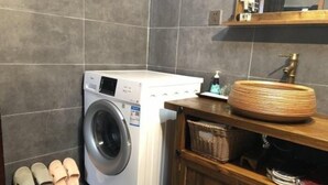 A laundry area with a washing machine, a sink, and a wooden cabinet with baskets.