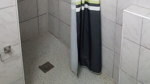 Un petit espace de douche carrelé, équipé d’un pommeau de douche, d’un pommeau de douche à main et d’un rideau.