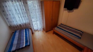 Une petite pièce comprenant un lit, un banc, une armoire et un téléviseur fixé au mur.