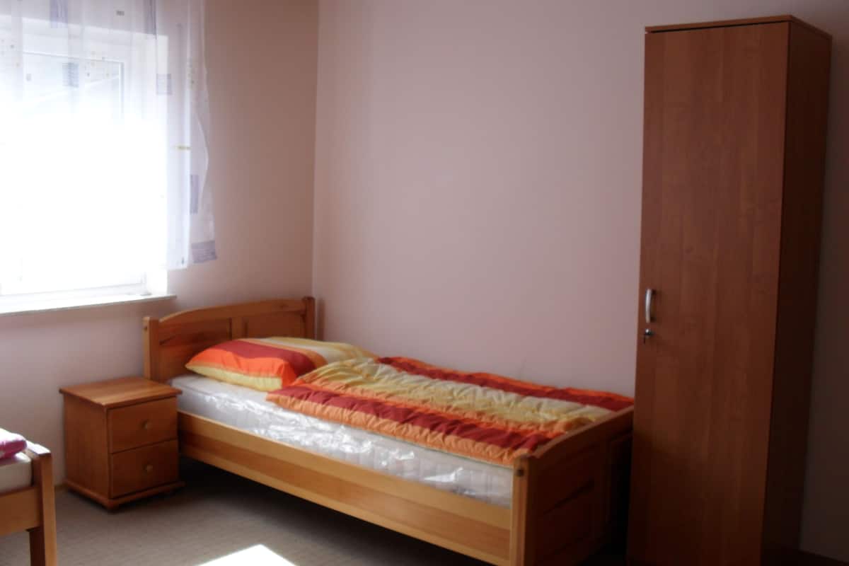 Ein Schlafzimmer mit einem hölzernen Bett, einem Nachttisch, einem Kleiderschrank und einem Fenster mit Vorhängen.