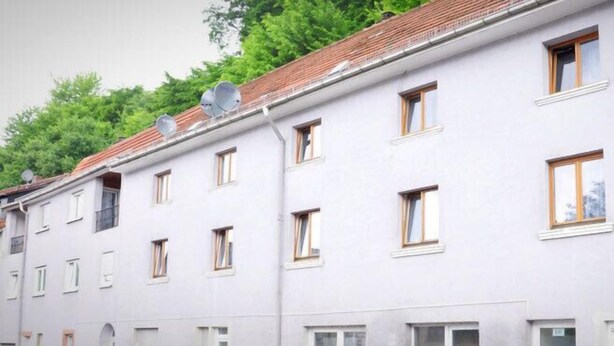 Un immeuble à plusieurs étages, doté d’une façade blanche, de nombreuses fenêtres et d’antennes paraboliques sur le toit.